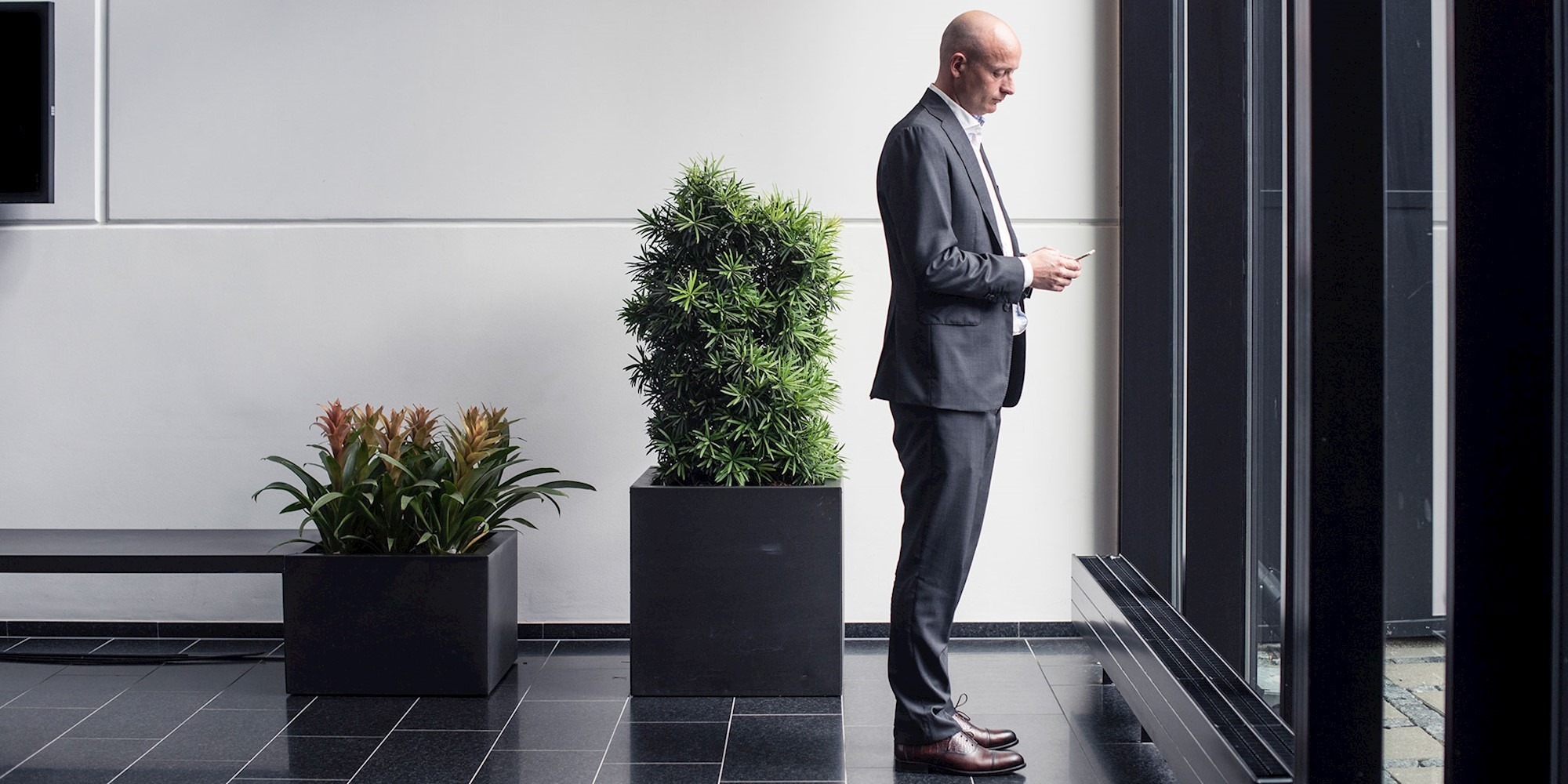 Man looking at his phone and standing in front of window